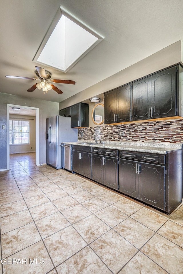 kitchen with appliances with stainless steel finishes, light countertops, a ceiling fan, backsplash, and a skylight