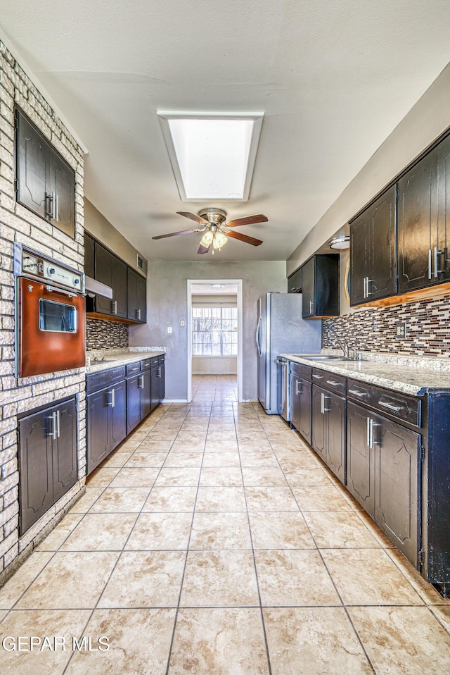 kitchen featuring light tile patterned flooring, a sink, wall oven, tasteful backsplash, and under cabinet range hood