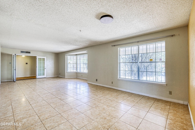 spare room featuring baseboards, a textured ceiling, visible vents, and light tile patterned floors