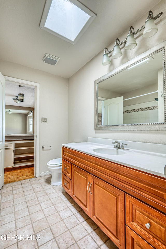 full bathroom with visible vents, a skylight, a shower, vanity, and toilet