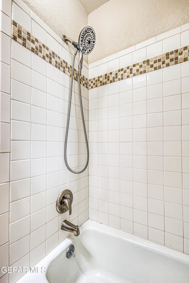 bathroom with a textured ceiling, a textured wall, and shower / washtub combination