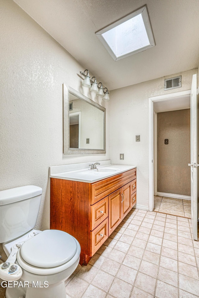 bathroom with a textured wall, vanity, toilet, a skylight, and visible vents