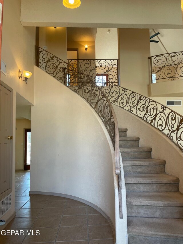 stairway with tile patterned flooring, visible vents, and a towering ceiling