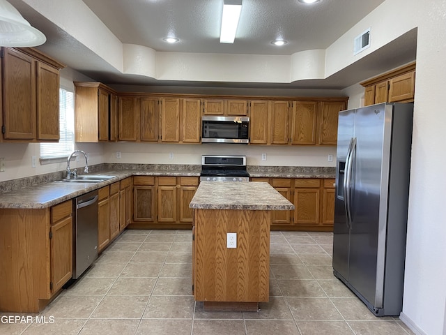 kitchen with visible vents, a kitchen island, brown cabinets, a sink, and appliances with stainless steel finishes