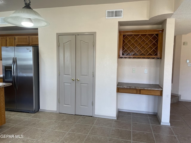 kitchen featuring brown cabinetry, visible vents, baseboards, stainless steel refrigerator with ice dispenser, and dark tile patterned flooring