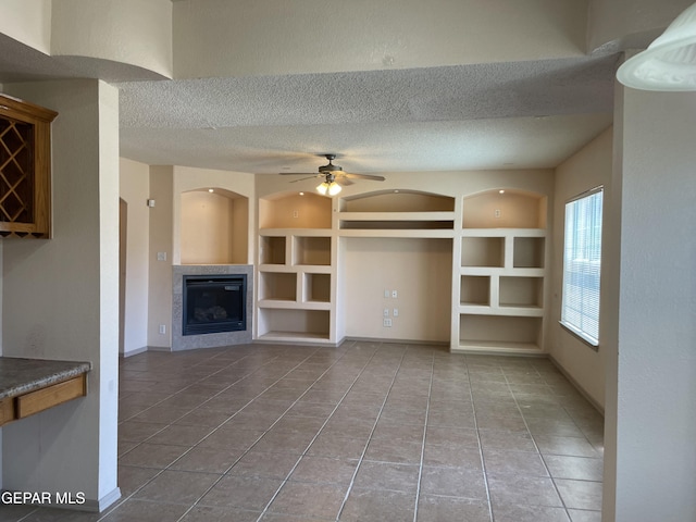 unfurnished living room with a fireplace, tile patterned floors, a textured ceiling, built in features, and a ceiling fan