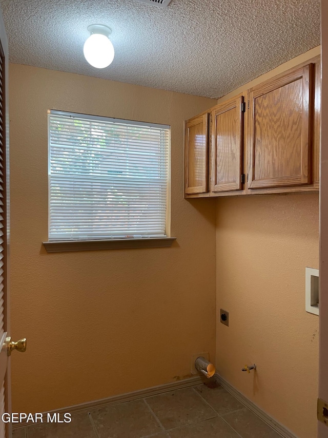 clothes washing area with a textured ceiling, cabinet space, tile patterned floors, and hookup for an electric dryer