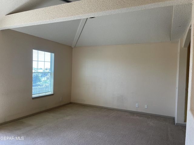 carpeted spare room featuring baseboards and vaulted ceiling