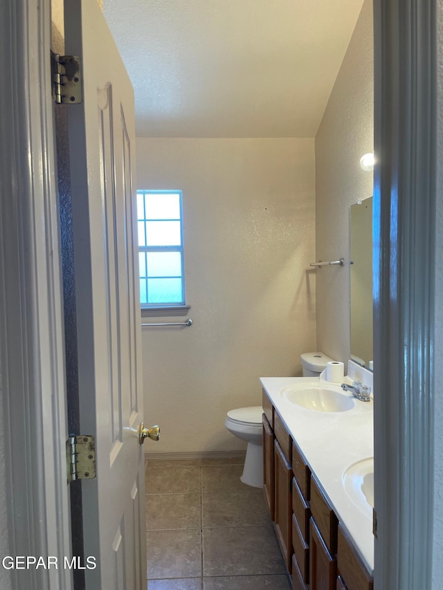 full bathroom featuring double vanity, a sink, tile patterned flooring, and toilet