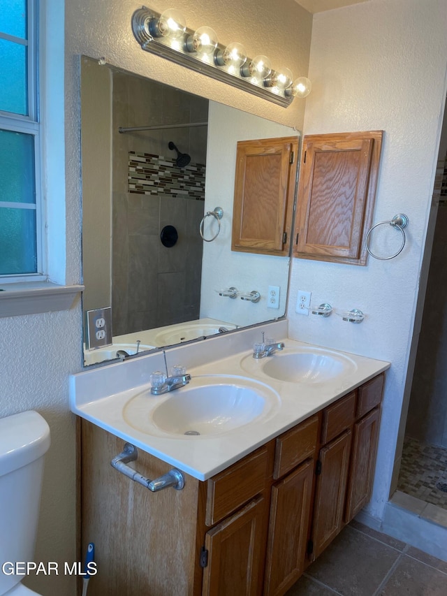 bathroom with double vanity, a sink, toilet, and tiled shower