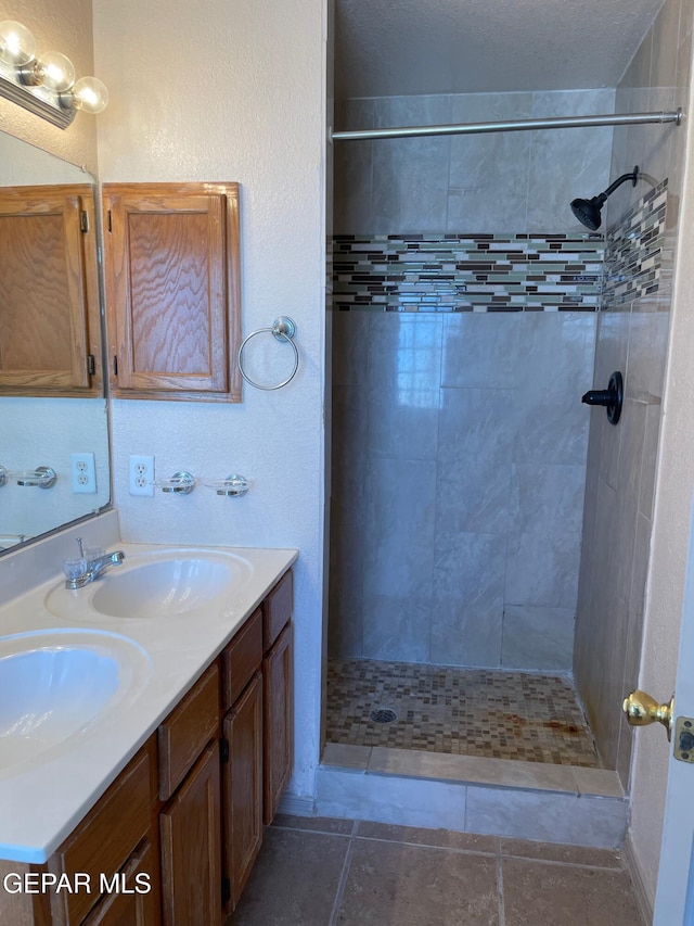 full bathroom featuring double vanity, tiled shower, and a sink