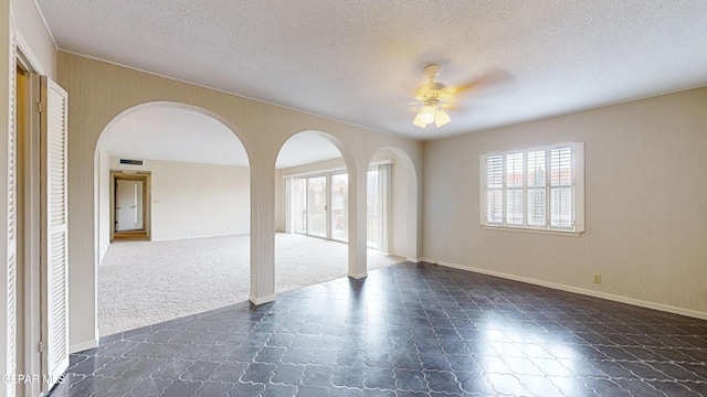 unfurnished room featuring a ceiling fan, a textured ceiling, arched walkways, baseboards, and visible vents