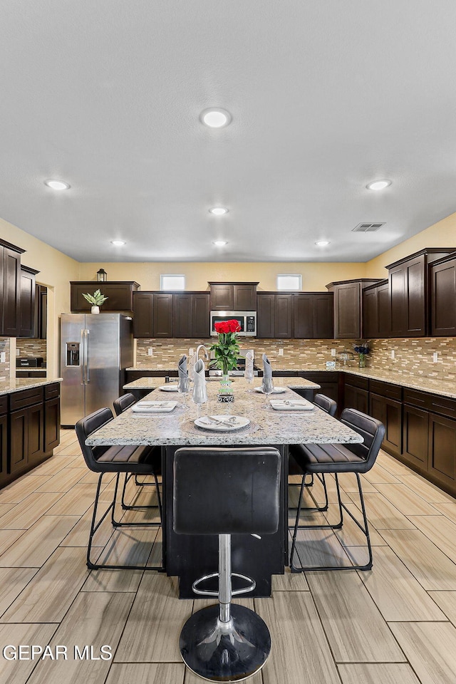 14717 Tierra Escape Ave, El Paso, TX 79938 - kitchen featuring stainless steel appliances, a breakfast bar, dark brown cabinetry, tasteful backsplash, and recessed lighting