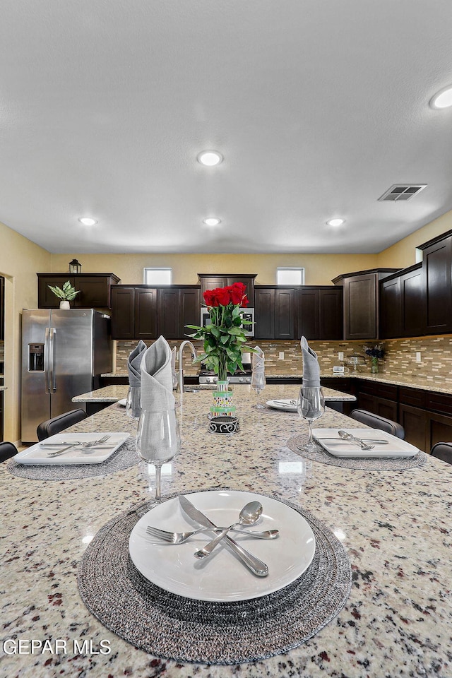 14717 Tierra Escape Ave, El Paso, TX 79938 - kitchen featuring stainless steel fridge with ice dispenser, decorative backsplash, light stone counters, dark brown cabinets, and recessed lighting