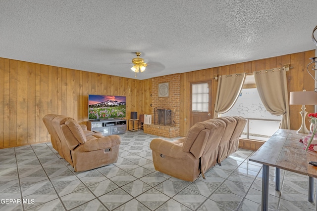 living room with a textured ceiling, a ceiling fan, light tile patterned flooring, wood walls, and a brick fireplace