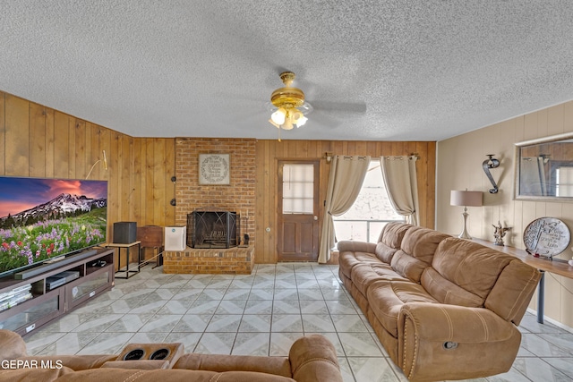 living area with wooden walls, a brick fireplace, a textured ceiling, and ceiling fan