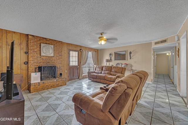 living area featuring visible vents, a ceiling fan, a textured ceiling, a fireplace, and wood walls