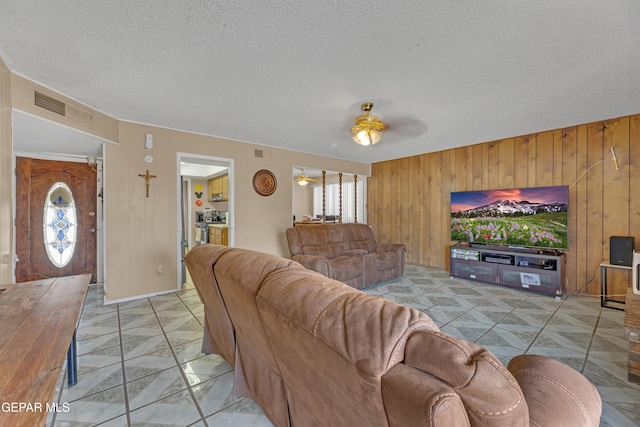 living room featuring a textured ceiling, wooden walls, a ceiling fan, and visible vents