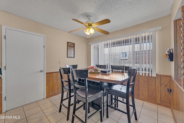 dining room featuring wooden walls, light tile patterned floors, a textured ceiling, a ceiling fan, and wainscoting
