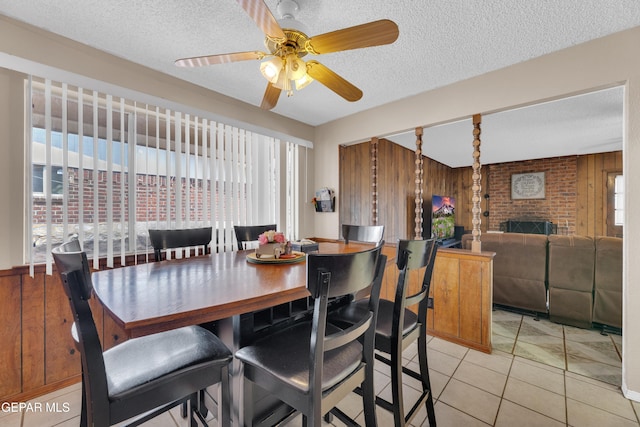 dining space featuring light tile patterned flooring, a textured ceiling, wood walls, and ceiling fan