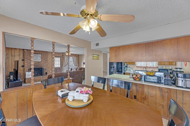 dining room with a brick fireplace, a textured ceiling, visible vents, and ceiling fan