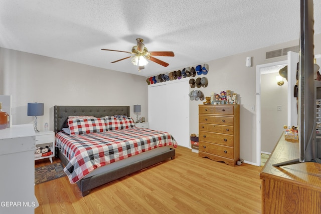 bedroom with visible vents, light wood-style flooring, ceiling fan, and a textured ceiling
