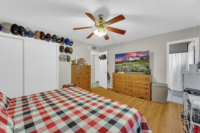 bedroom with a closet, light wood-type flooring, a textured ceiling, and a ceiling fan