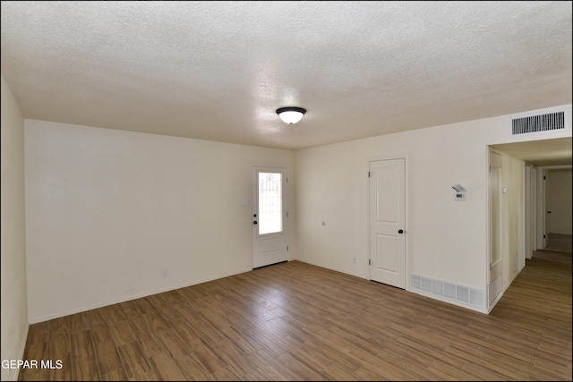 unfurnished room with wood finished floors, a textured ceiling, and visible vents