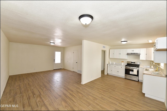 kitchen featuring open floor plan, light countertops, gas range, under cabinet range hood, and light wood-style flooring