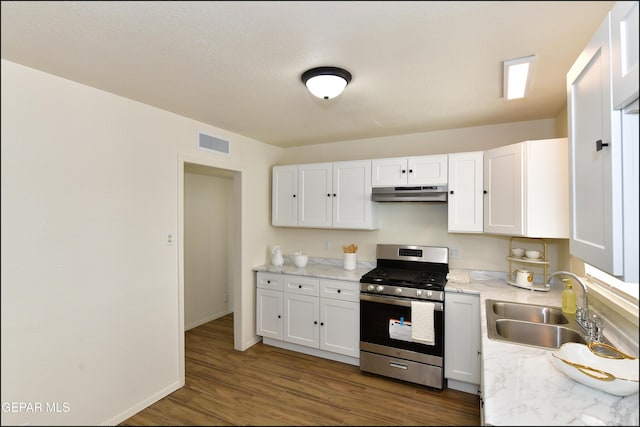 kitchen featuring visible vents, under cabinet range hood, white cabinetry, stainless steel gas range oven, and a sink