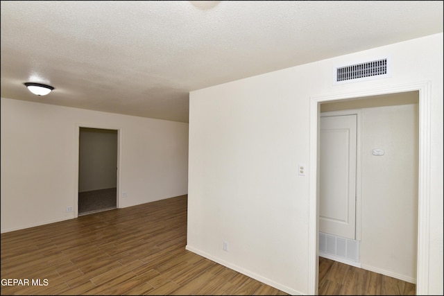 empty room with a textured ceiling, visible vents, and wood finished floors
