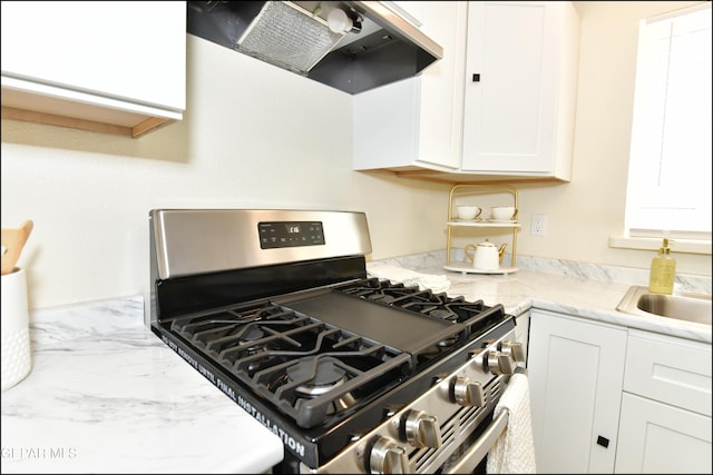 kitchen featuring light stone countertops, under cabinet range hood, white cabinetry, a sink, and gas range