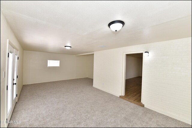 empty room with brick wall, light colored carpet, and a textured ceiling