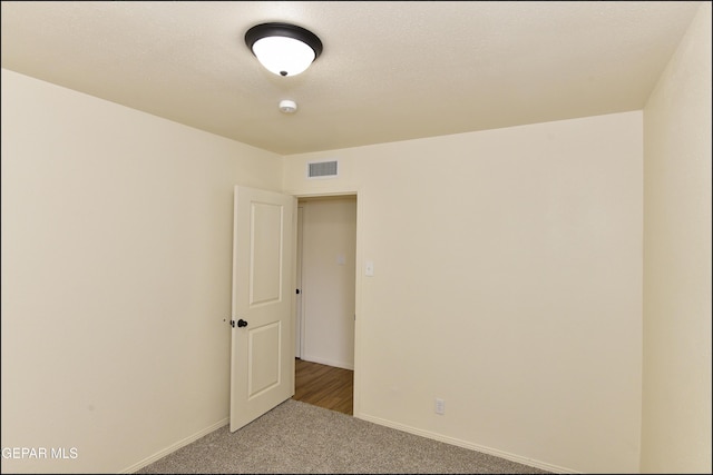 carpeted spare room with baseboards, visible vents, and a textured ceiling