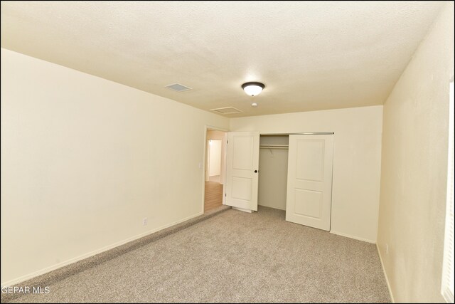 unfurnished bedroom featuring light colored carpet, baseboards, a textured ceiling, visible vents, and a closet
