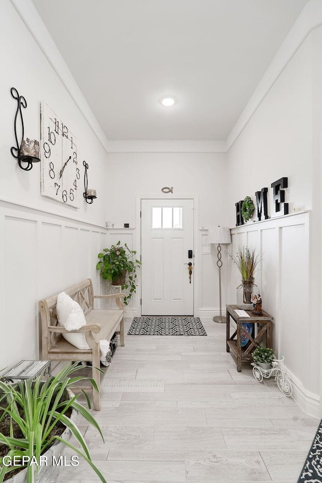 interior space with a decorative wall, wainscoting, crown molding, and wood finished floors