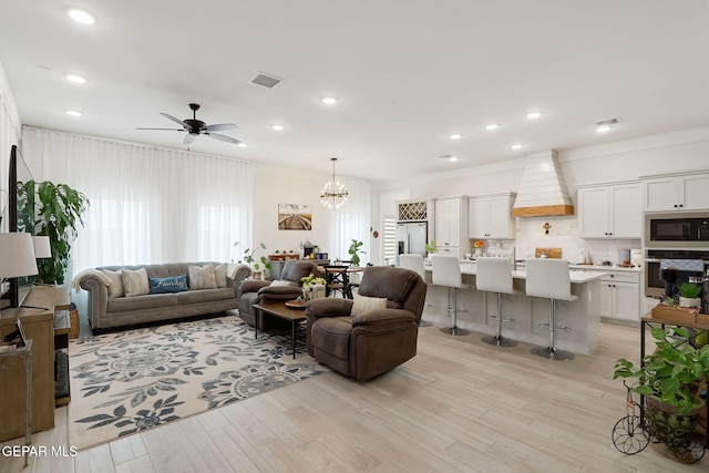 living area with light wood-style floors, ceiling fan with notable chandelier, visible vents, and recessed lighting