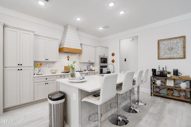 kitchen featuring light countertops, appliances with stainless steel finishes, a kitchen bar, custom range hood, and decorative backsplash
