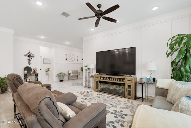 living room featuring a decorative wall, light wood-type flooring, ornamental molding, a ceiling fan, and visible vents