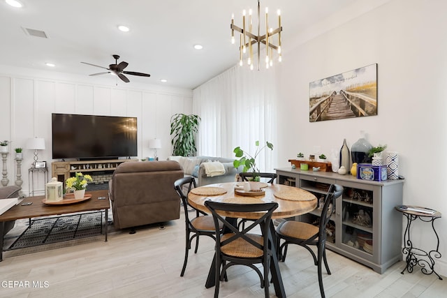 dining space with light wood-style flooring, ceiling fan with notable chandelier, visible vents, and recessed lighting