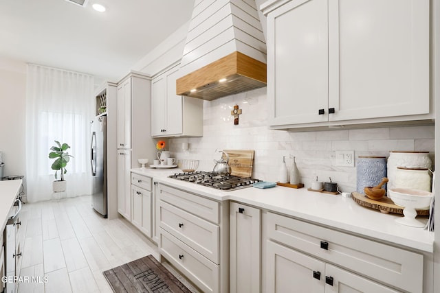kitchen with tasteful backsplash, white cabinets, light countertops, appliances with stainless steel finishes, and custom range hood