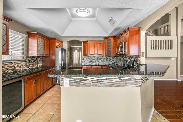 2987 Tierra Limon Dr, El Paso, TX 79938 - kitchen with wine cooler, a tray ceiling, appliances with stainless steel finishes, a peninsula, and glass insert cabinets