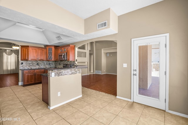 2987 Tierra Limon Dr, El Paso, TX 79938 - kitchen featuring stainless steel microwave, dark countertops, arched walkways, light tile patterned flooring, and lofted ceiling
