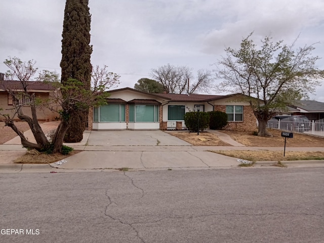 view of front of house featuring fence, brick siding, and concrete driveway
