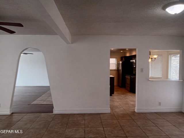 unfurnished room with beam ceiling, a ceiling fan, a textured ceiling, tile patterned flooring, and arched walkways