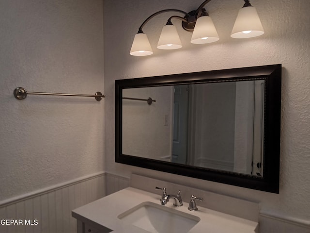 bathroom featuring vanity, a textured wall, and wainscoting