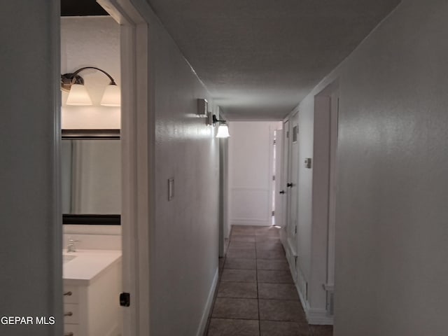 corridor featuring baseboards and dark tile patterned flooring