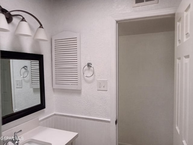 bathroom featuring a wainscoted wall, vanity, a textured wall, and visible vents