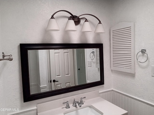bathroom with wainscoting, a textured wall, and a sink