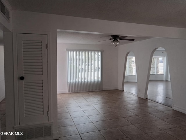 unfurnished room featuring tile patterned floors, baseboards, visible vents, arched walkways, and ceiling fan